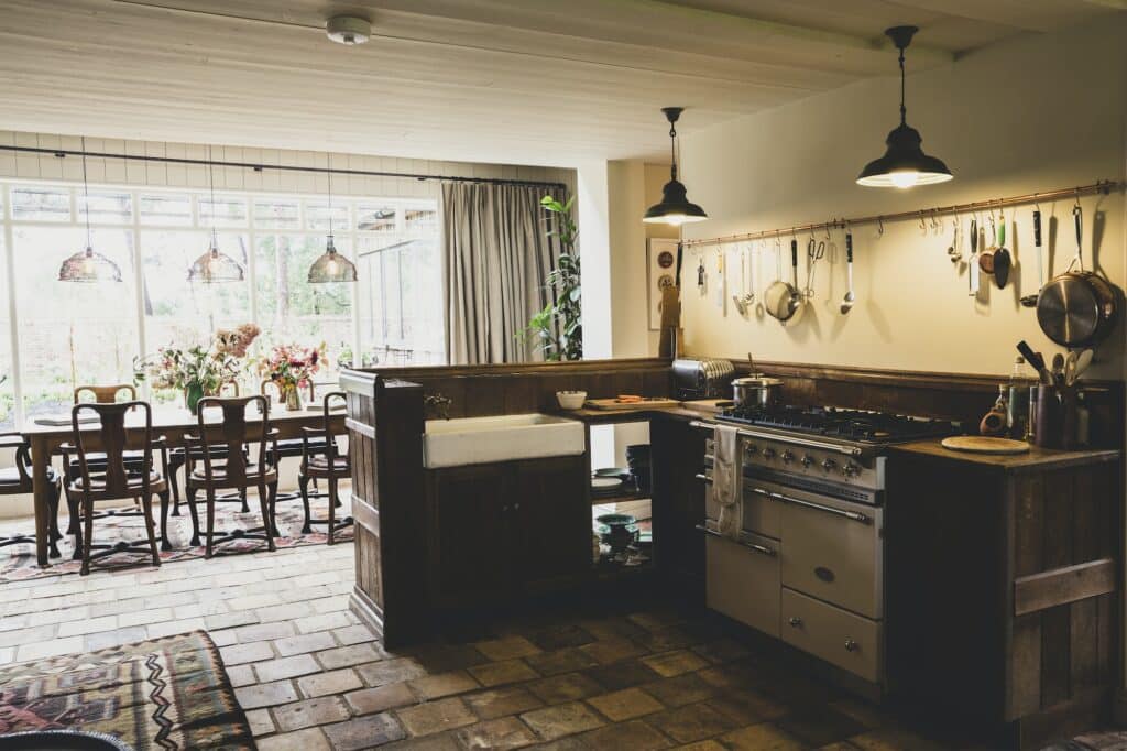 Interior view of kitchen with stone tile floor, range cooker and butler's sink, open plan to